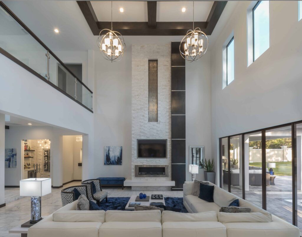 The living room of The Design Tourist's home features marble floors with grey veining, a 24-foot fireplace clad in white ledgestone and a custom crafted wood column with steel bands. The fireplace mantle has a cantilevered ledge of white quartz. The Design Tourist added a dose of cobalt blue with the shag rug and pillows mixing in textures of faux fur, leather, stone and wood. 