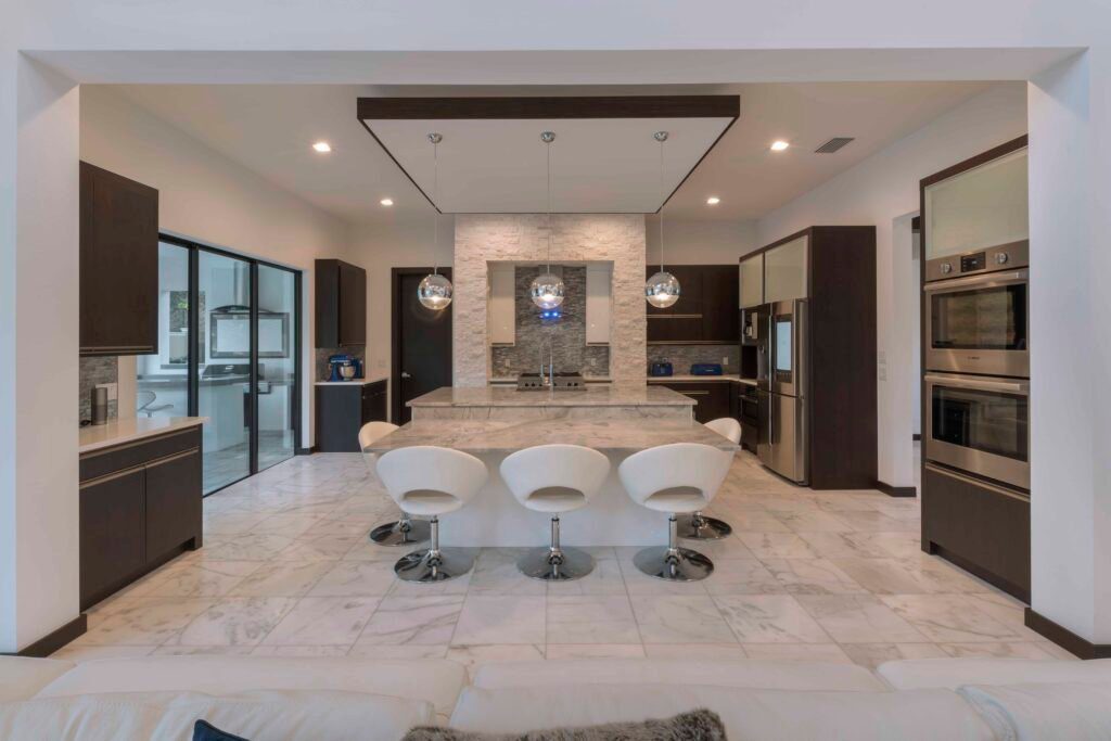 The grey and white color palette in The Design Tourist's kitchen plays with metallic accents including the silver glass tile backsplash that bounces light around the kitchen, chrome globe pendant lights, stainless steel appliances and chrome framed frosted glass upper cabinets. The quartz countertops around the perimeter of the kitchen and the quartzite double kitchen island give the space a contemporary feel that is grounded by espresso wood cabinets. 