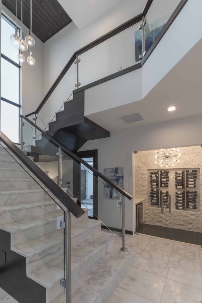 The glass and wood staircase in The Design Tourist's personal home features espresso wood handrails with chrome supports and marble stairs with mitered wood cladding on the sides. 