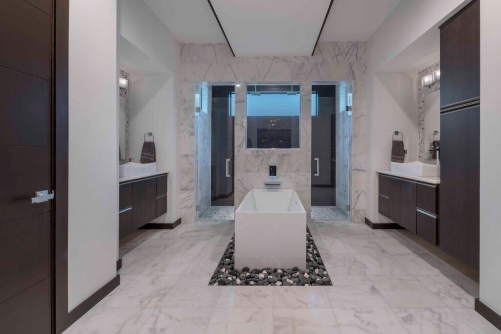 The master bathroom in The Design Tourist's personal residence draws inspiration from boutique hotels with a zen/spa-like ambiance created with natural elements including a bed of river rocks below the freestanding tub and porcelain shower tile that mimics the look of espresso wood used throughout the home. 