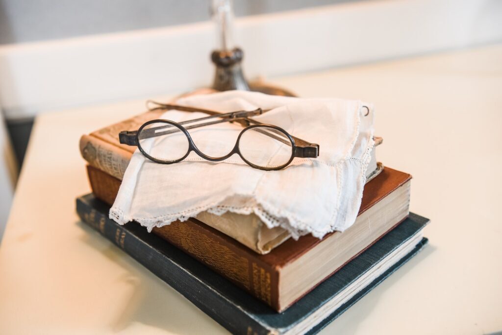 Antique glasses, a handkerchief, and books on a nightstand.