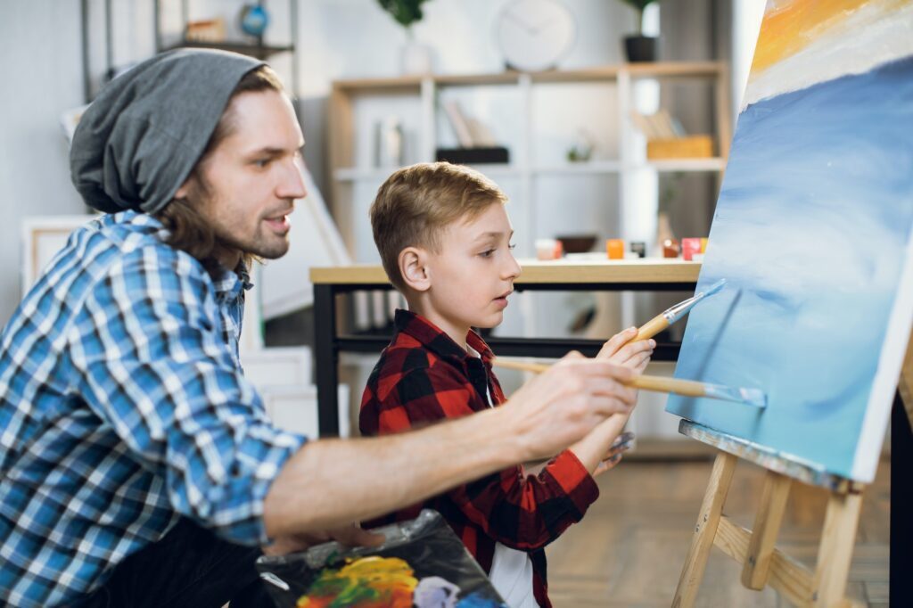 Teacher and schoolboy painting with brushes on canvas