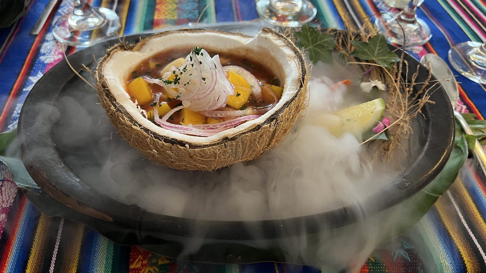 Ecuadorian ceviche served in a coconut shell with rising smoke on a colorful woven cloth