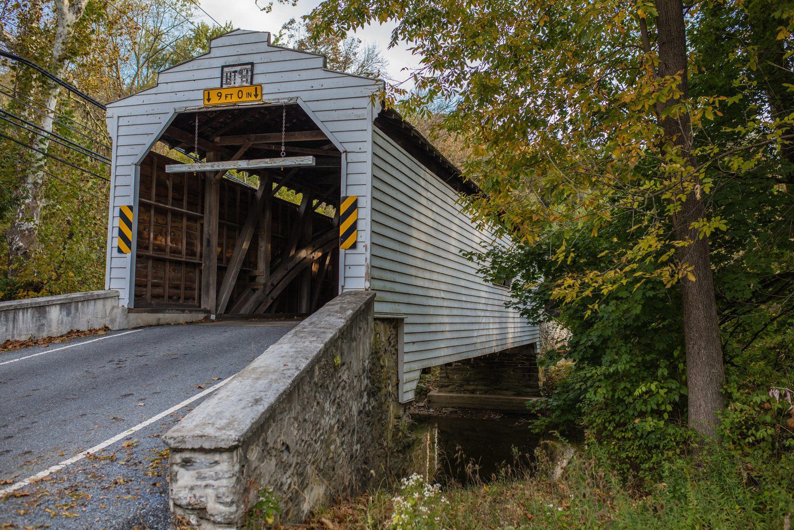 White-painted covered bridges with a 9-foot clearance sign in Chester County, Pennsylvania, surrounded by trees and fall foliage.