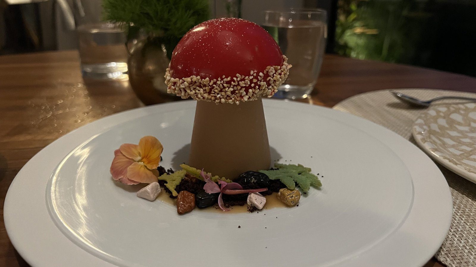 Whimsical mushroom-shaped dessert topped with sesame and surrounded by edible flowers at 1906 Restaurant