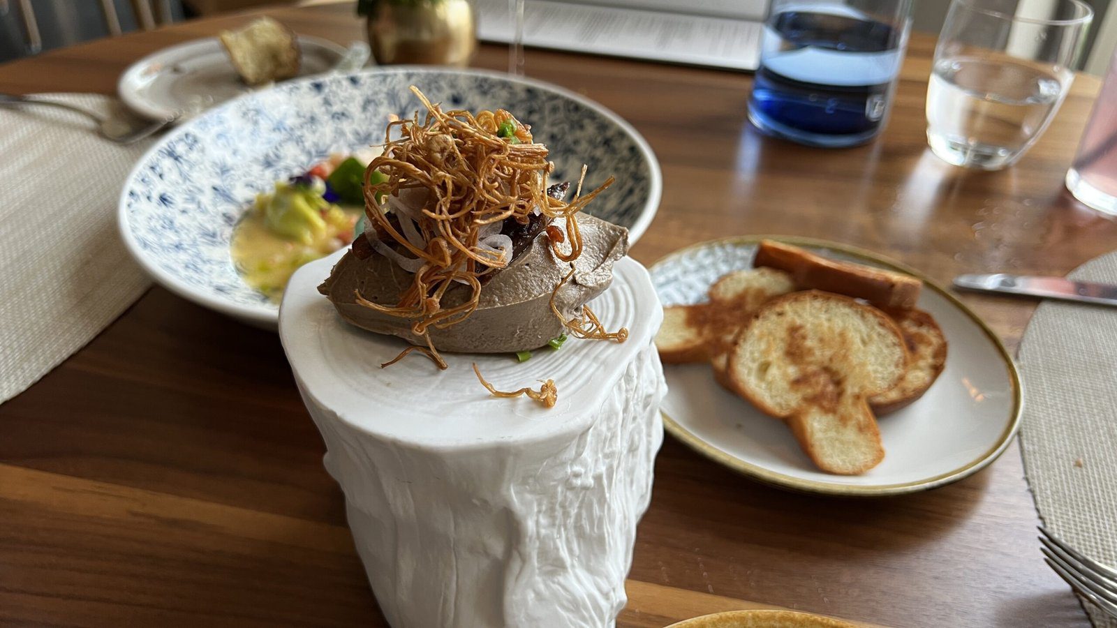 Artfully plated appetizer on a white ceramic pedestal at 1906 Restaurant, surrounded by toasted baguette slices and salad