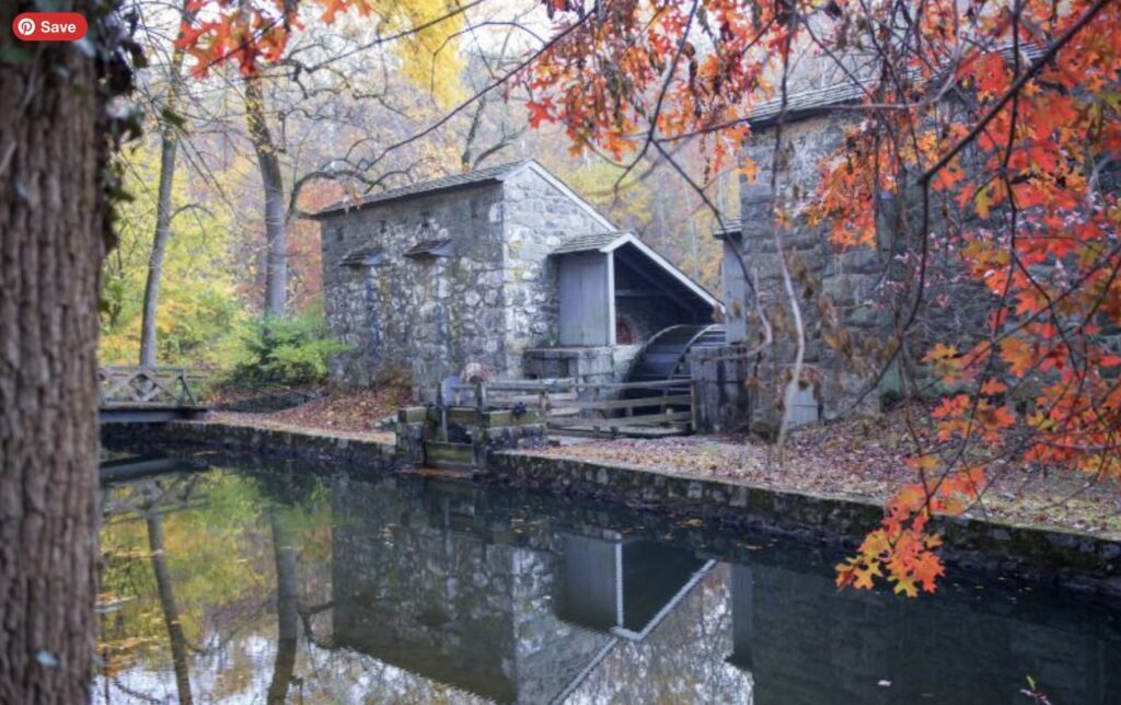 Stone water mill with turning wheel reflected in a peaceful canal during autumn at Hagley Museum