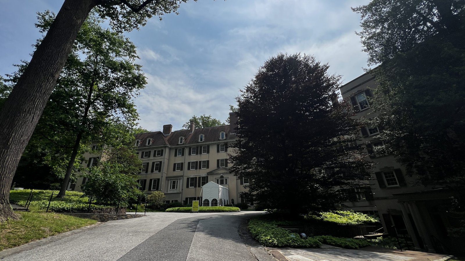 Front driveway leading to the historic Winterthur Museum and Gardens, shaded by mature trees under a summer sky
