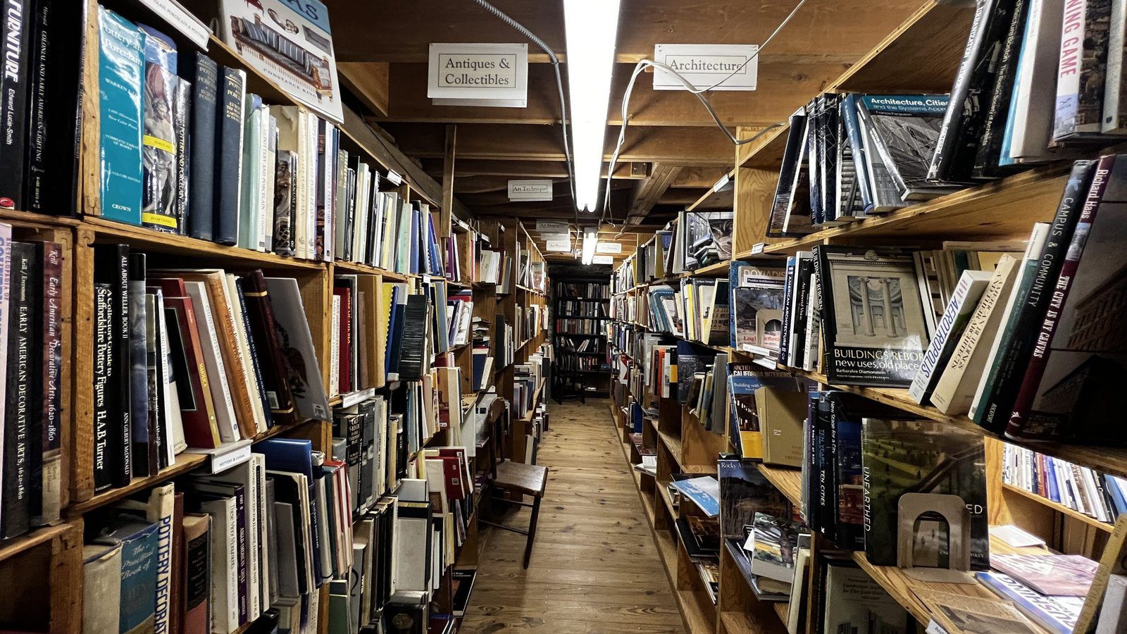 Long aisle of tightly packed books at Baldwin’s Book Barn, with category signs above and wooden floors below, showcasing the depth of Brandywine Valley’s best bookstores.
