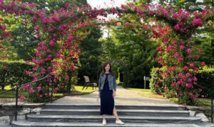 Woman posing beneath a blooming rose-covered archway on stone steps at Longwood Gardens