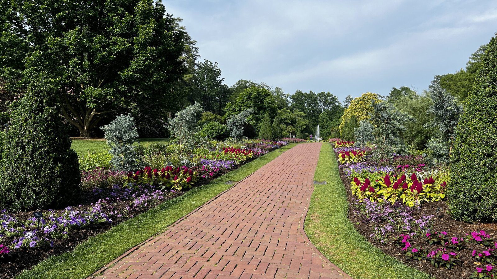 Brick path lined with colorful flowerbeds and trees in the gardens at Longwood Gardens