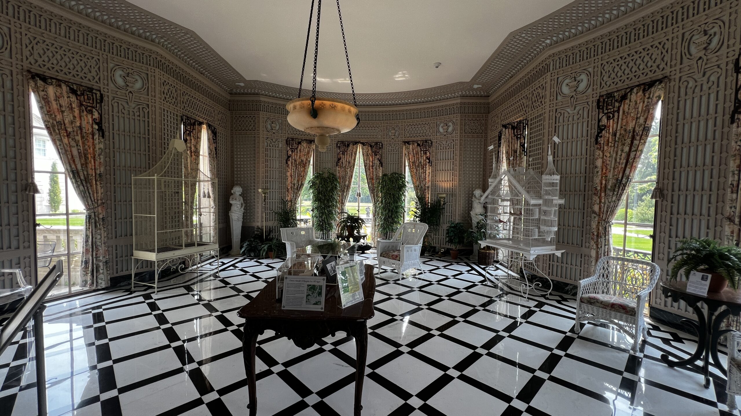Bright solarium room in Nemours Estate with checkered tile floor, birdcages, and wicker seating