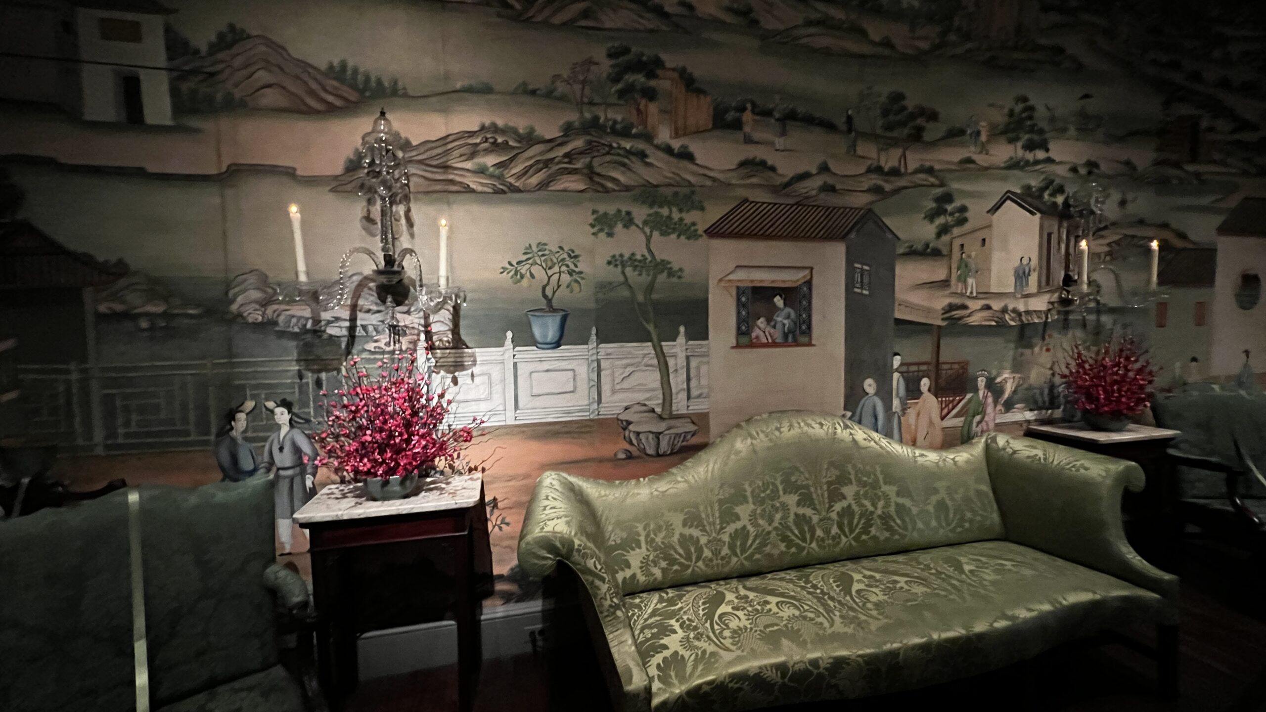 Close-up of hand-painted Chinese wallpaper with landscape scenes and a green antique sofa at Winterthur