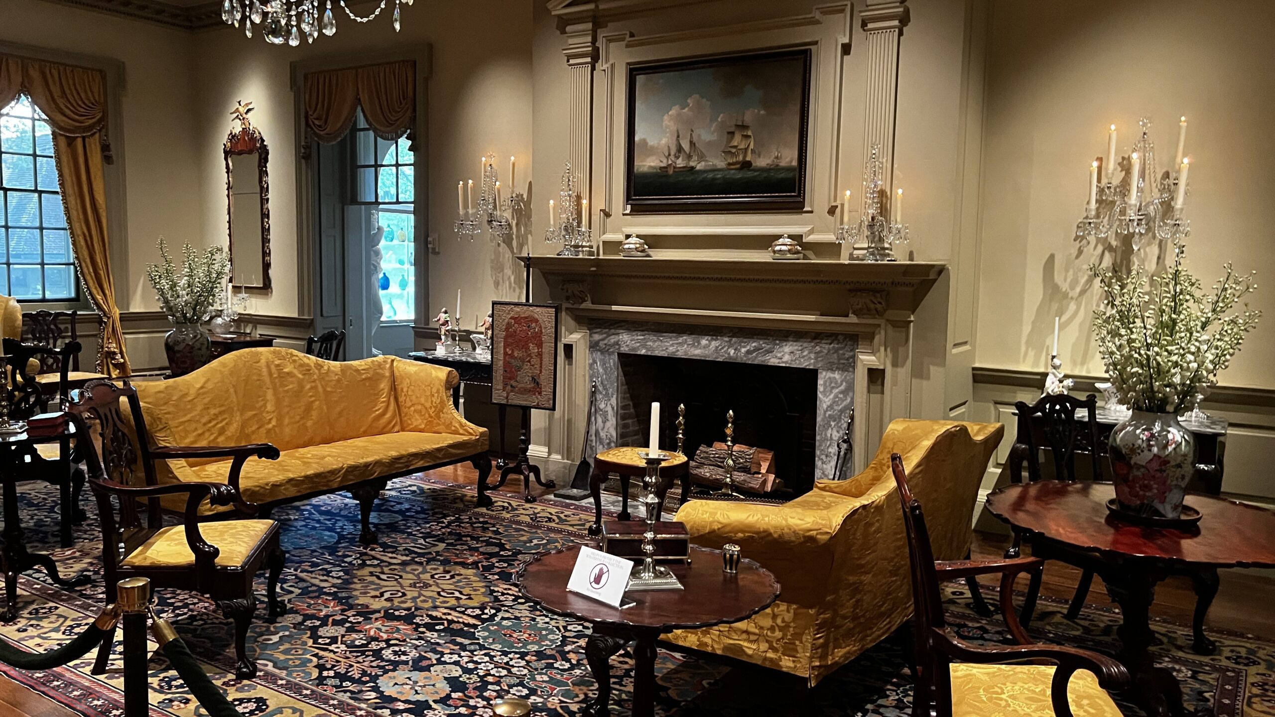 Full view of the yellow parlor at Winterthur with ornate fireplace, candle sconces, and 18th-century furnishings