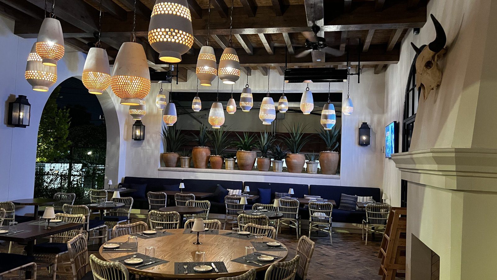 Stylish outdoor dining room at Latuli in Houston’s Memorial neighborhood, featuring woven pendant lights, terracotta planters, and rustic wood beams.