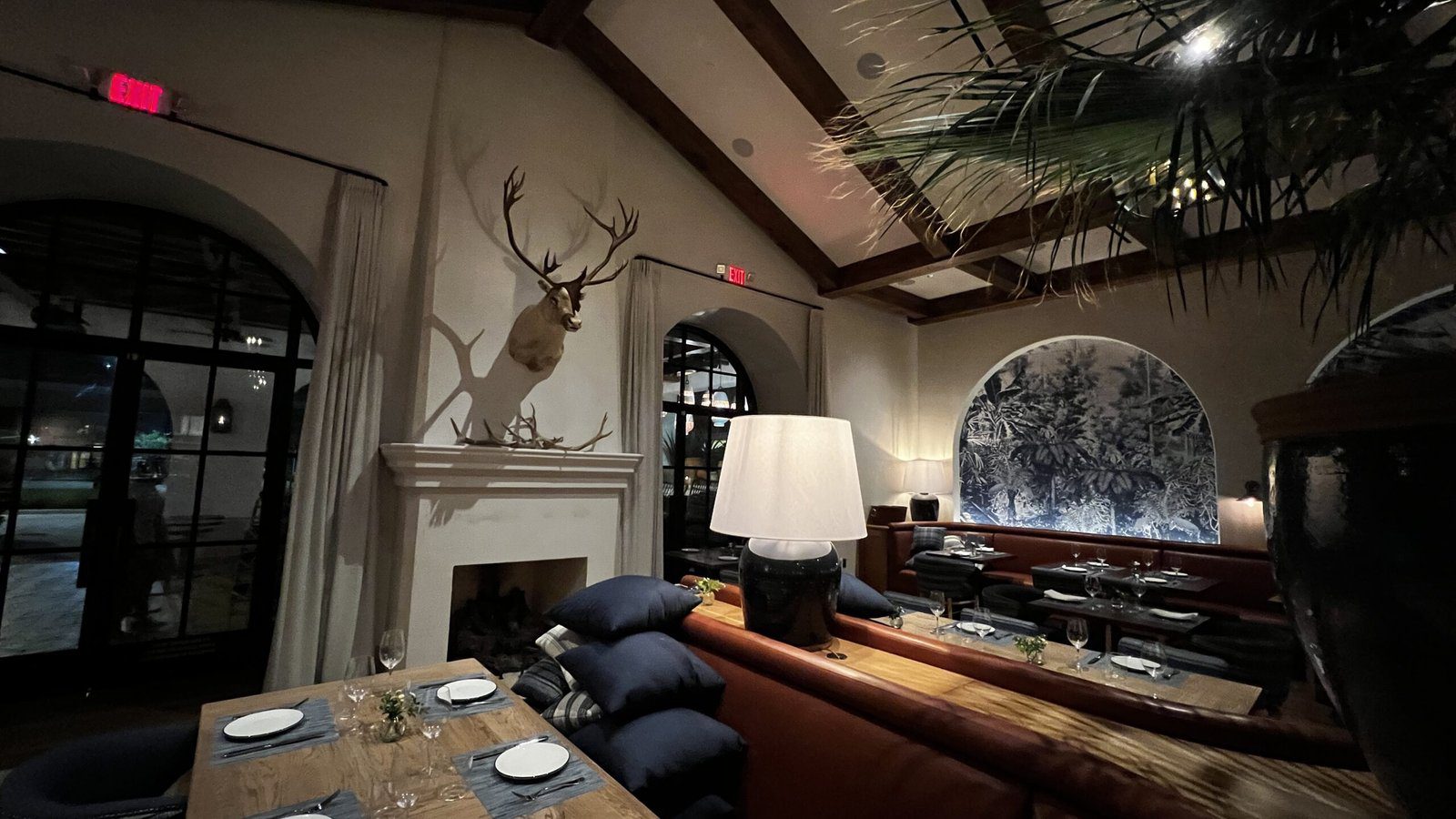 Cozy interior of Latuli with vaulted ceilings, deer mount above the fireplace, and elegant seating accented by a botanical mural.