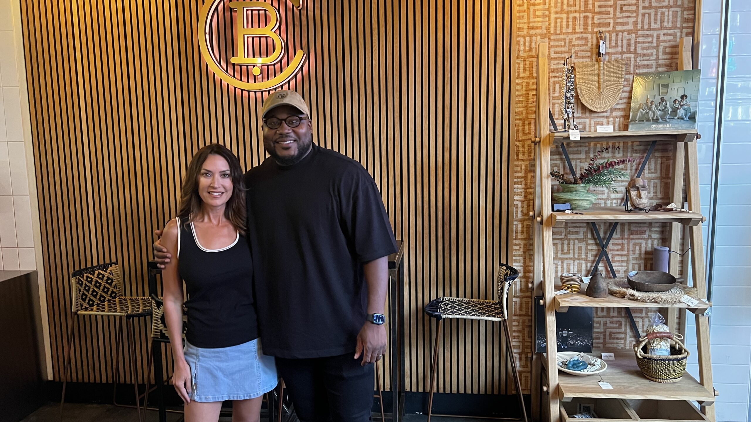 Chef Ope Amosu, founder of Chopnblok, standing beside a guest inside POST Houston with a display of artisanal goods in the background.