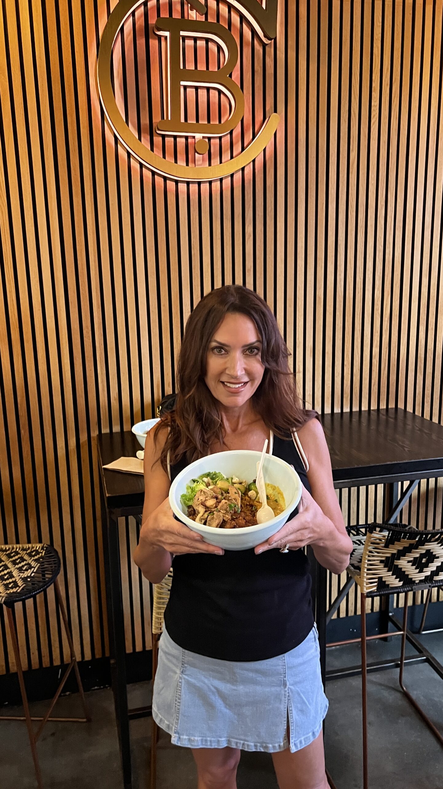 Woman holding Chopnblok’s Golden Bowl, a Nigerian-inspired dish with grilled chicken, curry, and spiced vegetables, inside POST Houston.