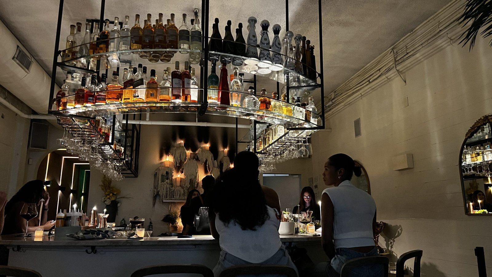 Stylish bar at Clarkwood in Houston with illuminated hanging liquor shelves and guests enjoying drinks beneath warm lighting.