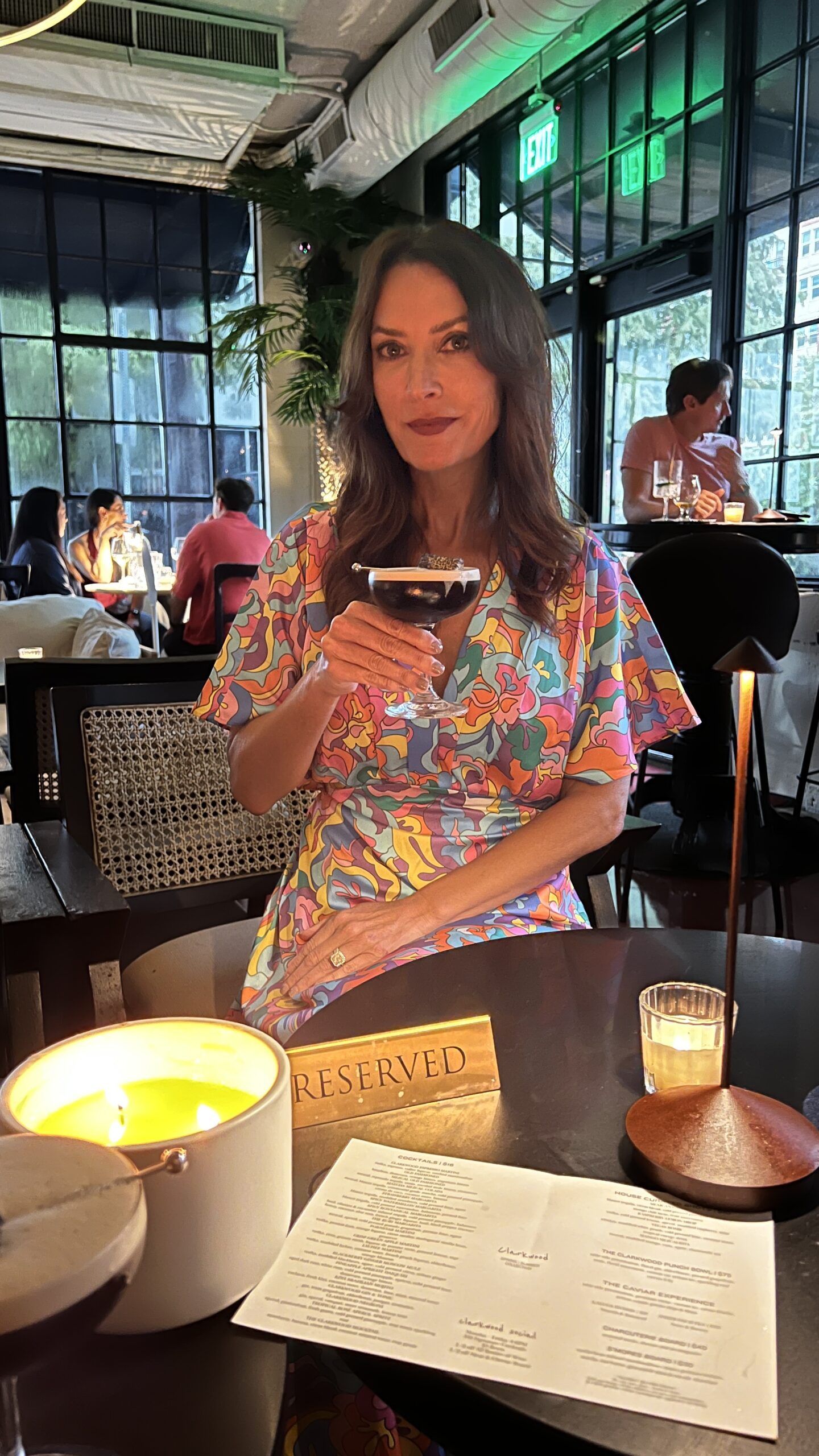 Woman seated at Clarkwood in Houston holding the signature espresso martini beside a candlelit reserved table sign.