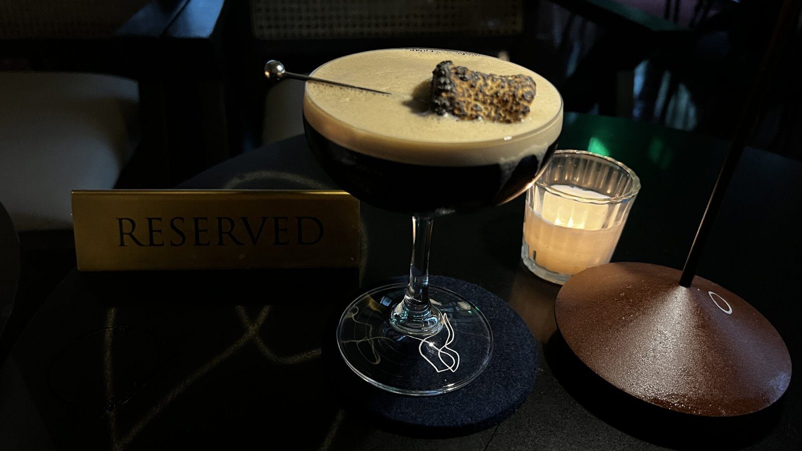 Espresso martini at Clarkwood in Houston, topped with a toasted marshmallow and served beside a candlelit reserved table sign—experiencing culinary culture in Bayou City.