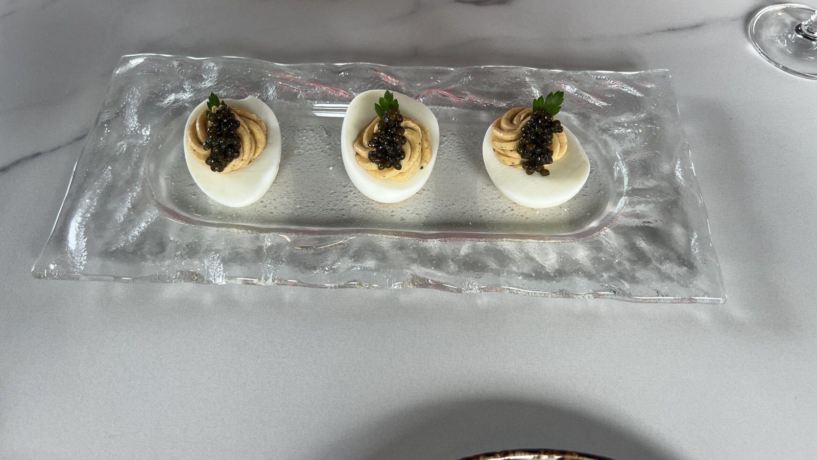 Elegant deviled eggs topped with caviar and herbs on a glass serving tray at Maven.