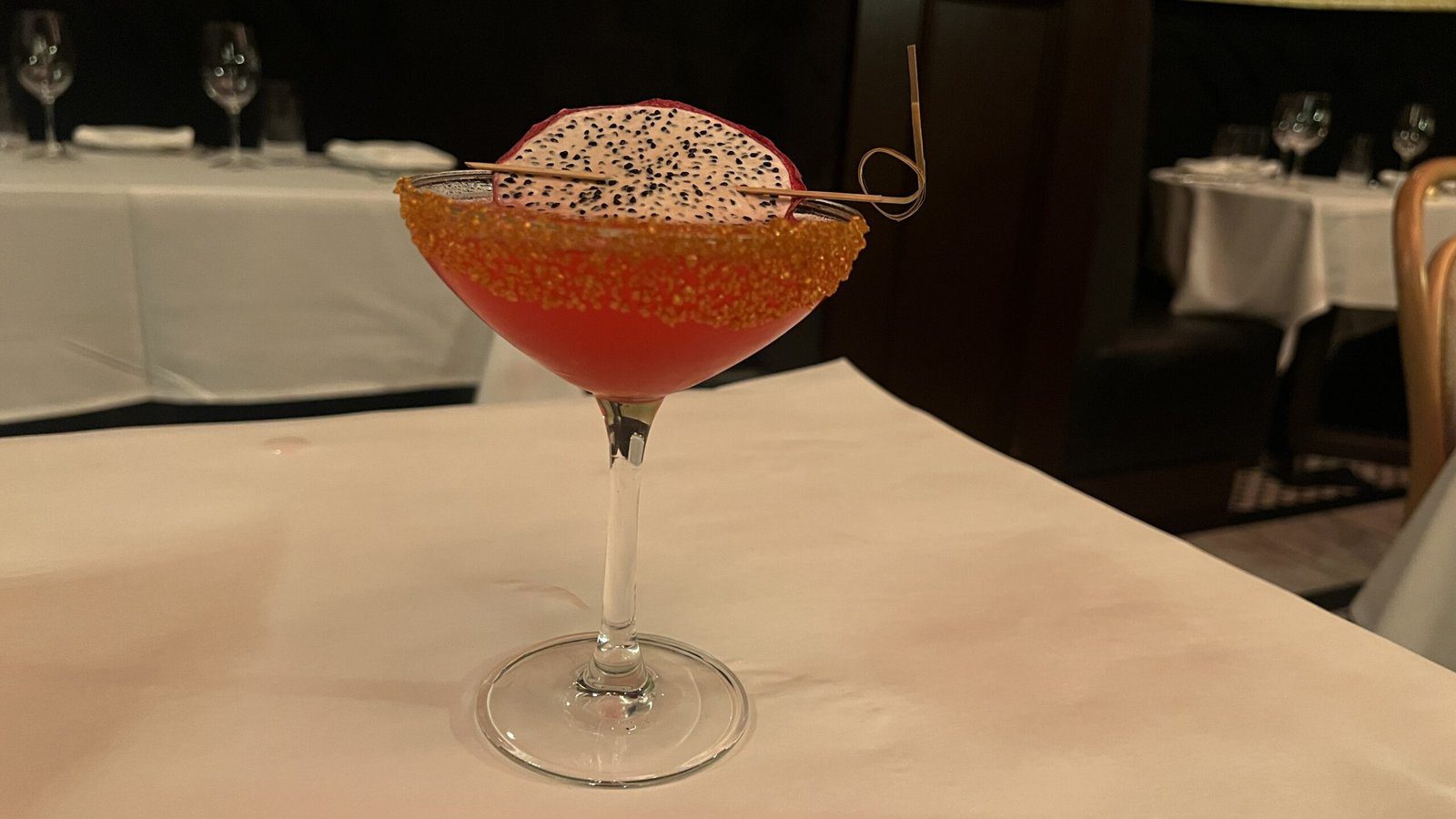Cosmobelle cocktail at Annabelle Brasserie, garnished with dragonfruit and served in a glass rimmed with orange sugar crystals.