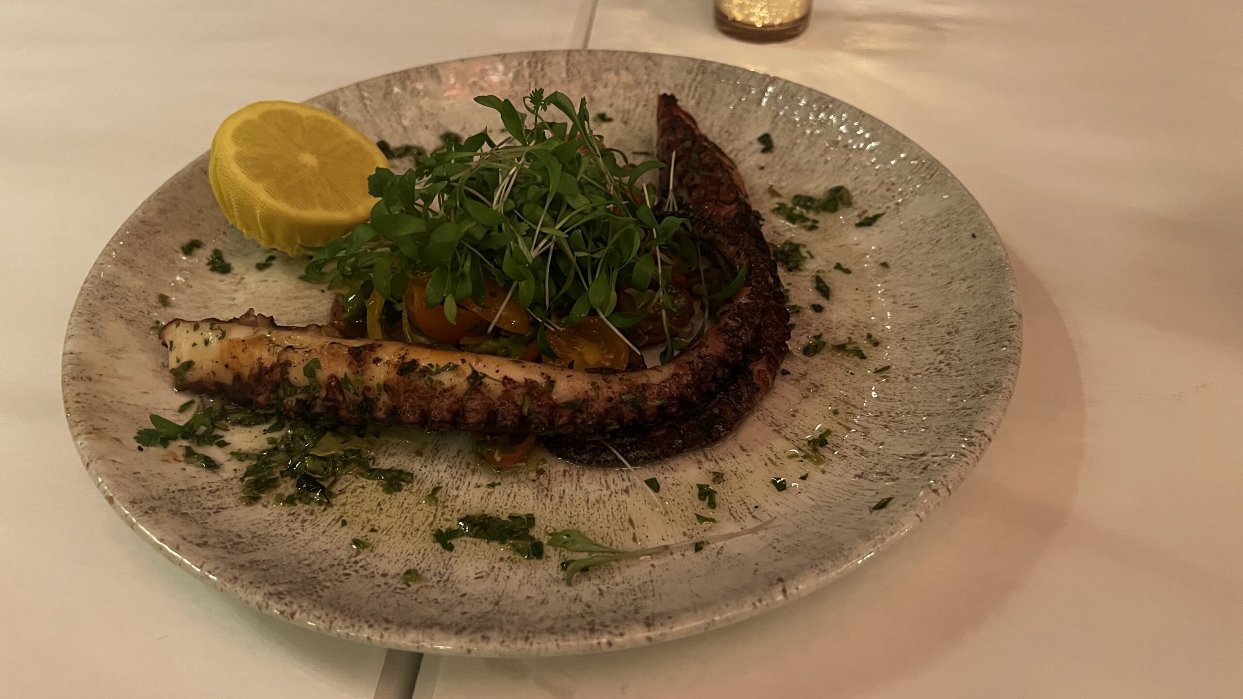 Plate of grilled octopus served with fresh greens, cherry tomatoes, and a lemon wedge at Annabelle Brasserie in Houston.