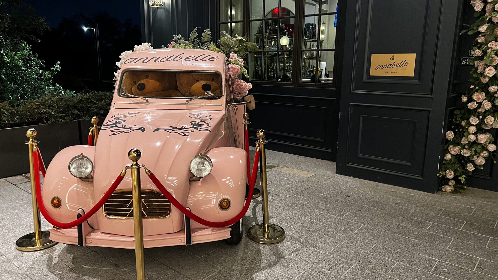 Vintage pale-pink Citroën car decorated with flowers and oversized teddy bears at the entrance of Annabelle Brasserie in Houston’s Autry Park.