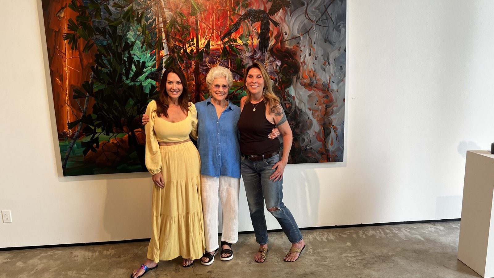 Three women standing together smiling in front of a large abstract painting at Betty Moody Gallery in Houston.