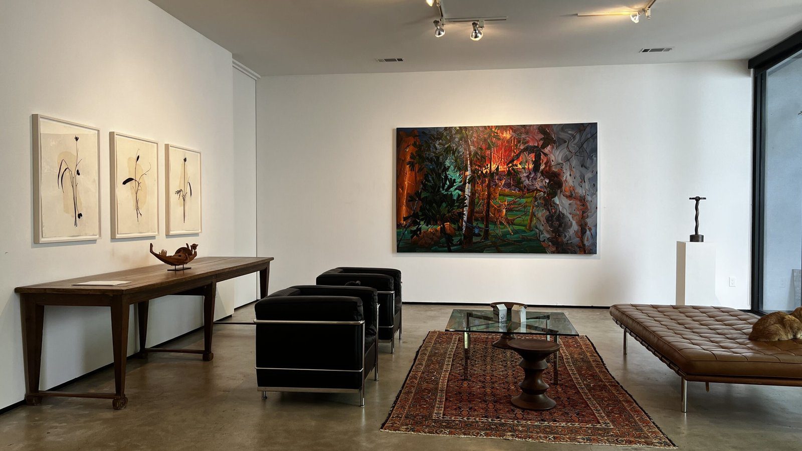 Contemporary gallery interior with black chairs, wood table, and Melissa Miller’s large forest-inspired painting on the wall.