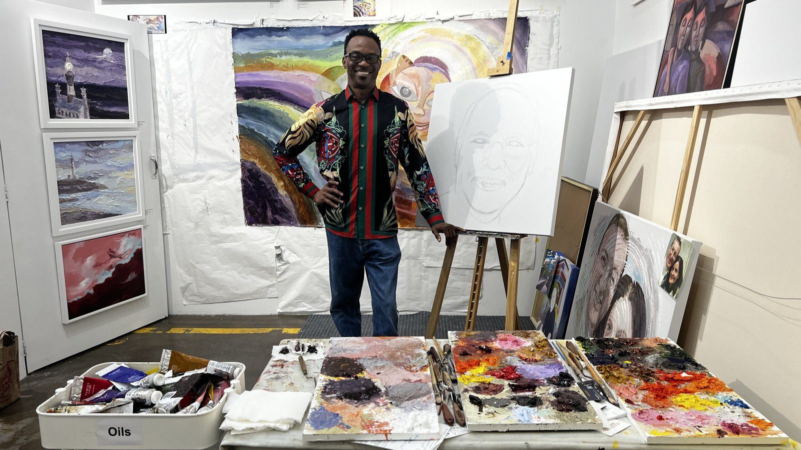 Artist Chu Okoli standing in his Silver Street Studios workspace surrounded by oil paints, canvases, and colorful works in progress.