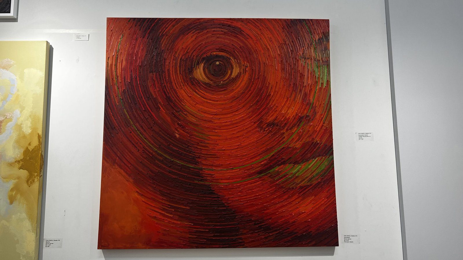 Large abstract red painting with concentric swirls forming a partial face, displayed on a gallery wall.