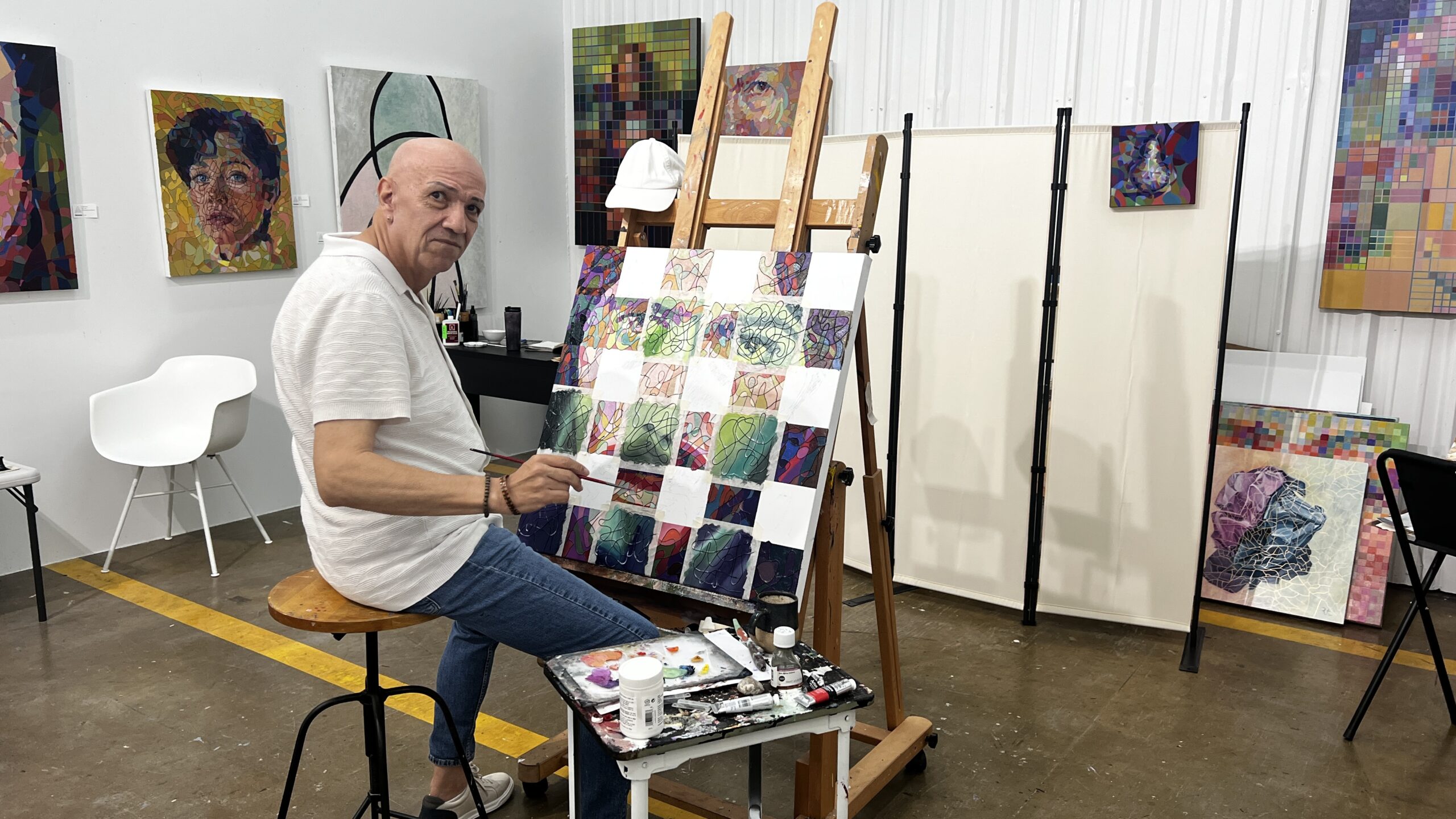 Artist Rodrigo Aguilera seated at an easel painting colorful mosaic-style squares inside his studio at Sawyer Yards.