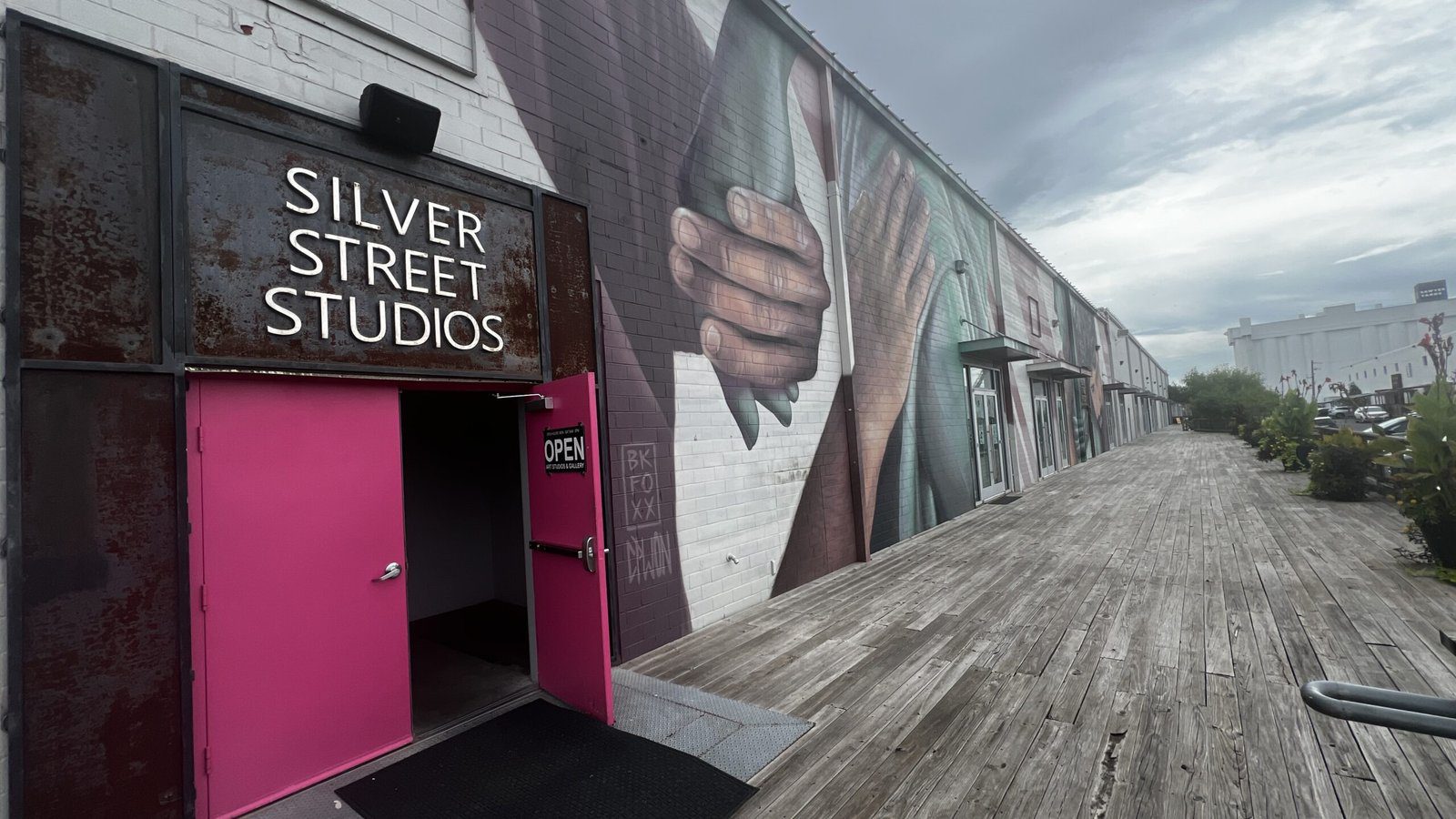 Entrance to Silver Street Studios at Sawyer Yards with bright pink doors and large mural of hands on the warehouse wall.