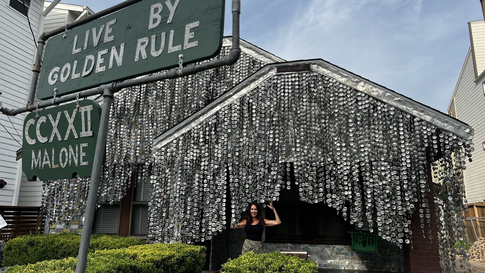Beer Can House in Houston covered in flattened aluminum can siding, with a woman standing at the entrance under a sign reading “Live by Golden Rule.”