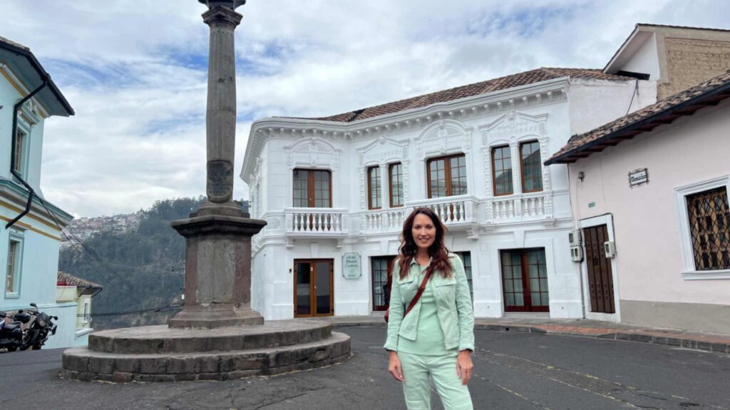 A woman wearing a light green suit standing in front of the ornate white colonial facade of Hotel Mama Cuchara in the historic La Loma Grande neighborhood of Quito Ecuado