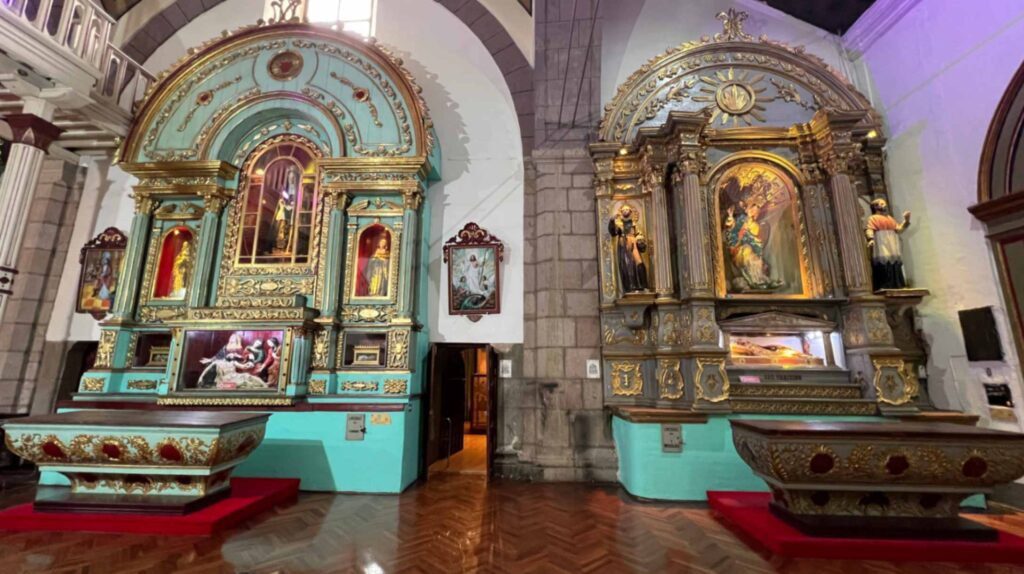 Interior view of a historic church in Quito showing two large ornate altars with gold leaf details one painted bright teal and the other left in a classic gold finish alongside religious statues