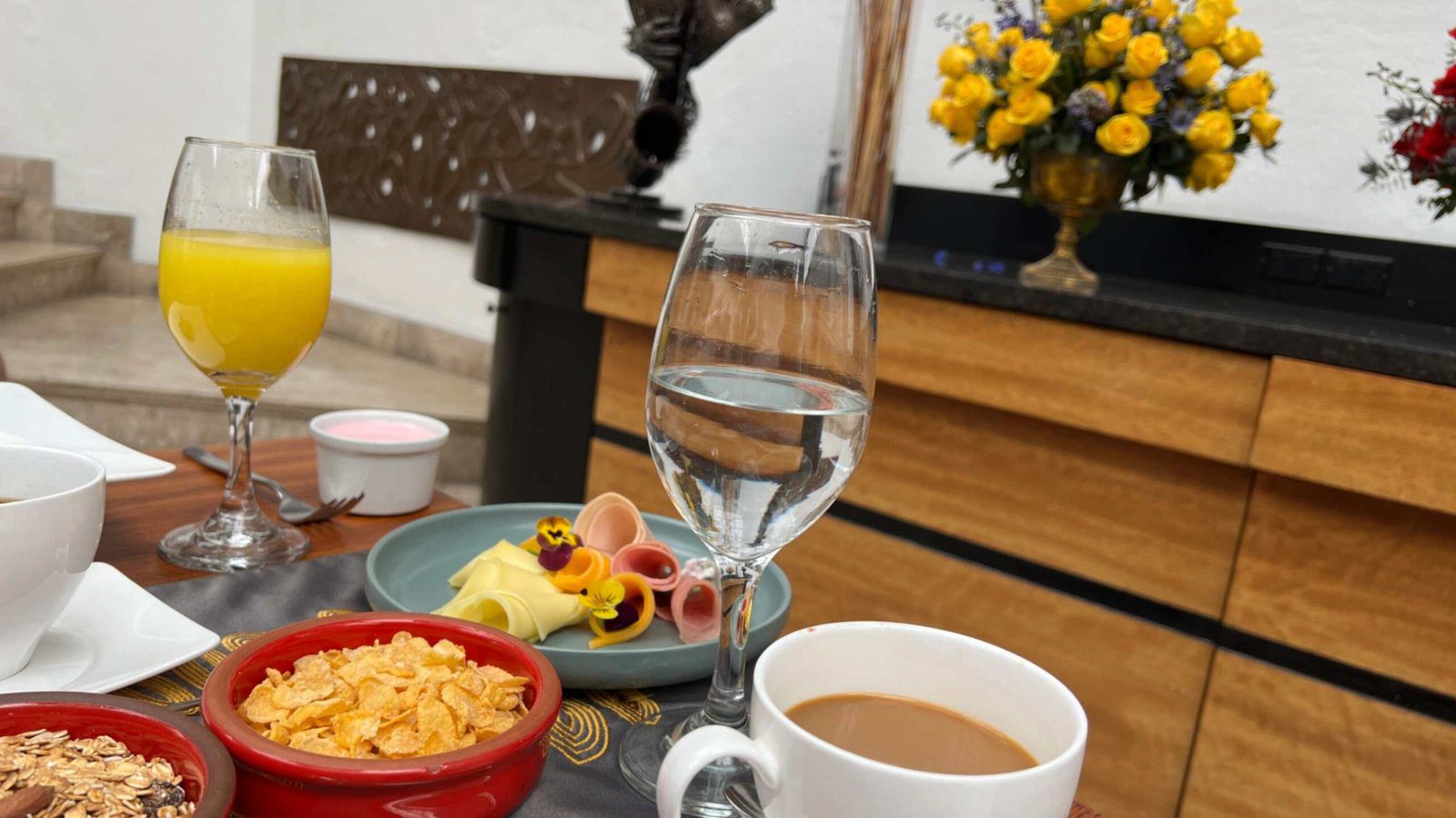 A curated breakfast buffet table at a boutique hotel in Quito showcasing fresh juice coffee bowls of cornflakes and rolled ham and cheese slices decorated with edible flowers